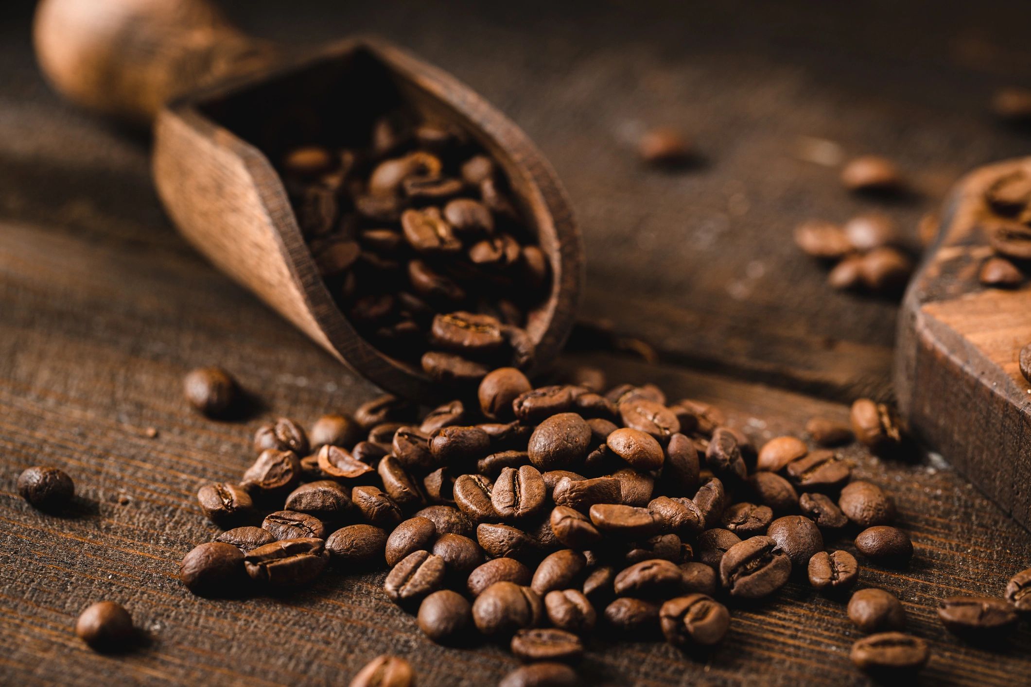 Roasted coffee beans in a wooden scoop on a rustic table