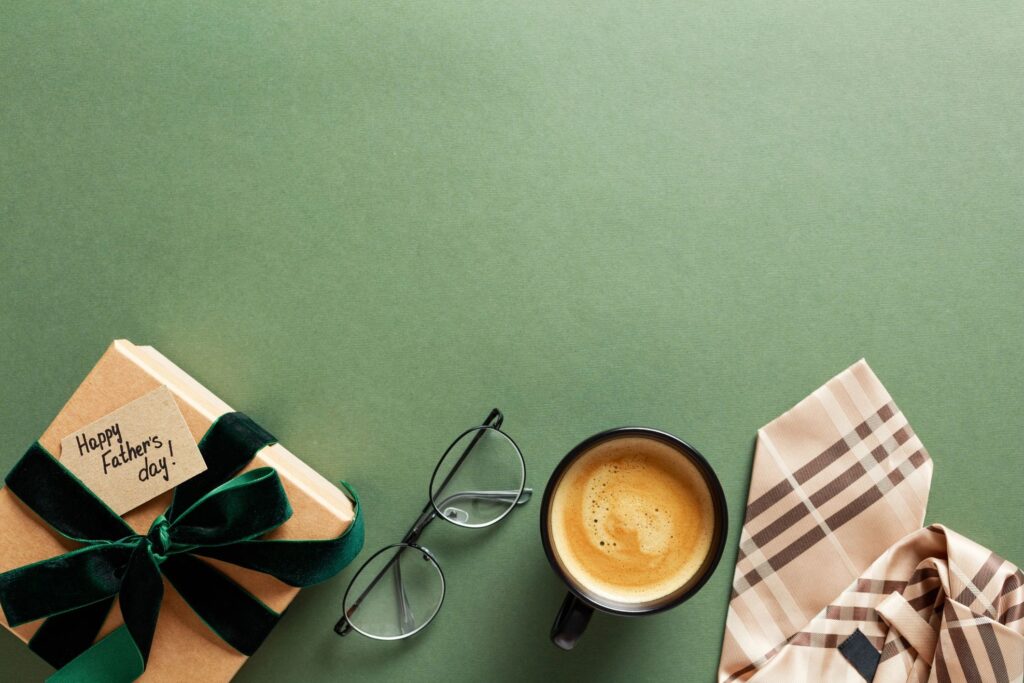 Fathers Day gift on green table with necktie, glasses, and cup of coffee. Vintage style. Top view.