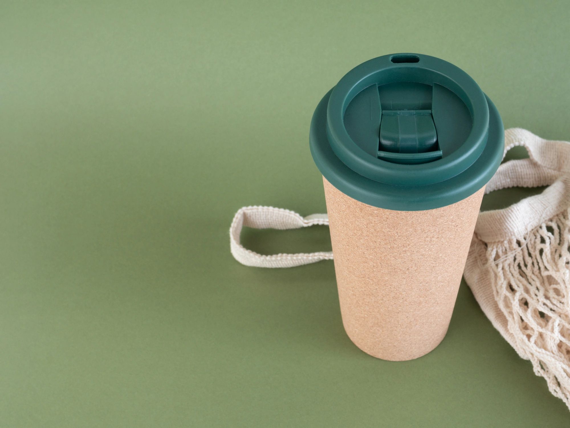 Reusable cup and cloth bag on green background