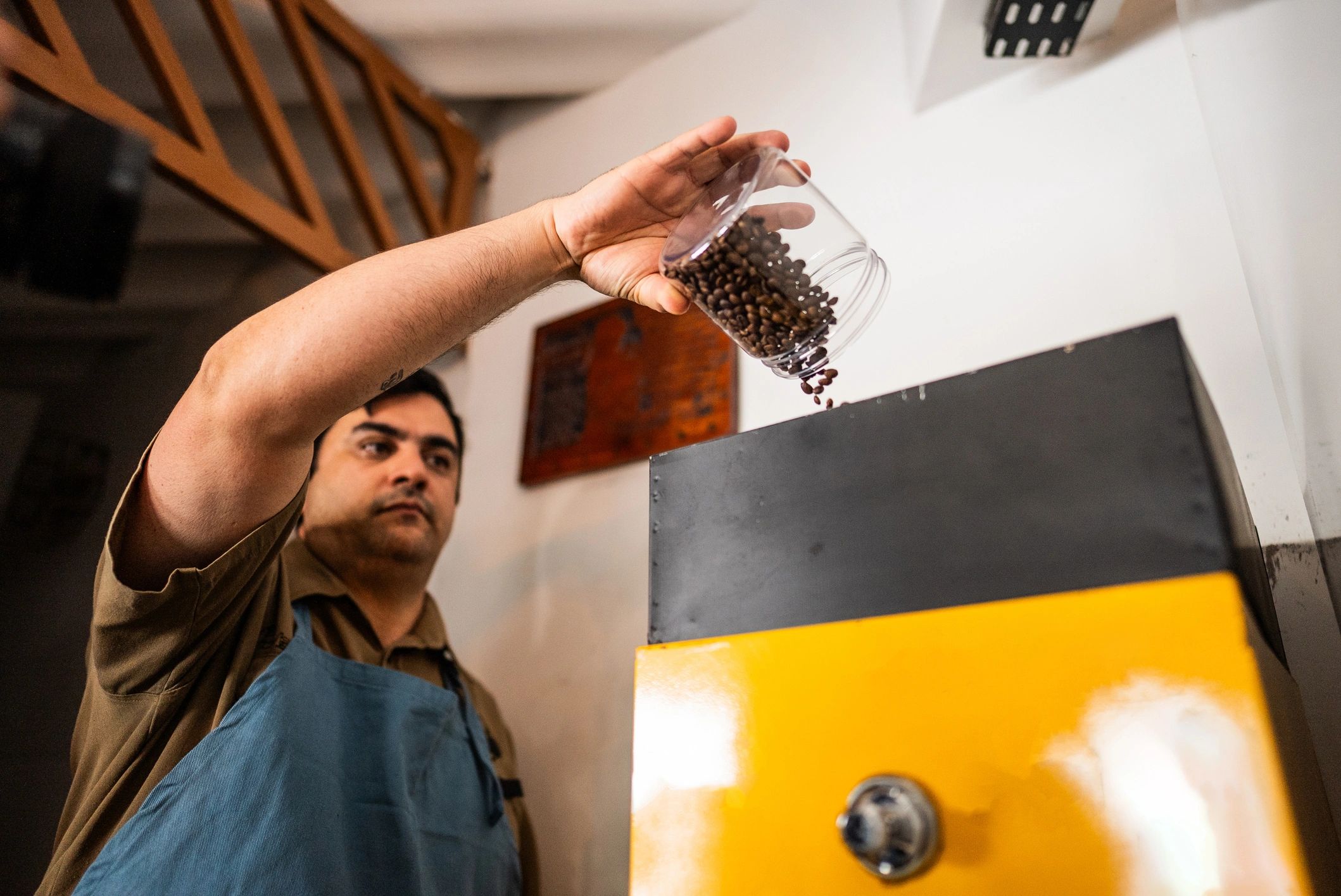 Hands pouring coffee beans into a grinder in a coffee shop